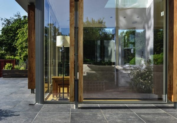 Home Extension. The lower third of the frame is a stone patio, the upper two thirds show a portion of the glazed extension, inside a seating area can be seen. Communion Architects Herefordshire.