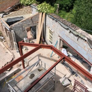 View from above, showing a red steel frame of a new extension, in the background is former extension, made from breeze blocks being reimagined.
