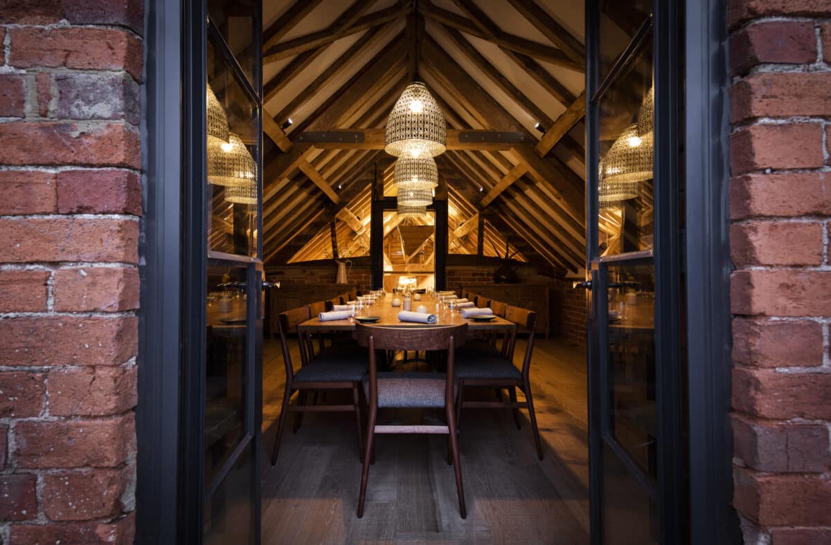 Private upstairs dining room at bensons restaurant, long central table with wood chairs along it, with an apex roof and exposed timber beams. A rustic and elegant atmosphere by candle light. Communion Architects Herefordshire