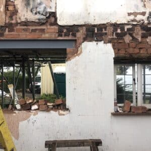 Photo of the exterior wall from a fire damaged cottage. The wall shows to window sections. The Left hand section has had the top lintel replaced with a steel version. The original timber lintel can still be seen above the right hand frame. The lintels are damaged by fire and rot so are being replaced. Communion Architects Herefordshire.