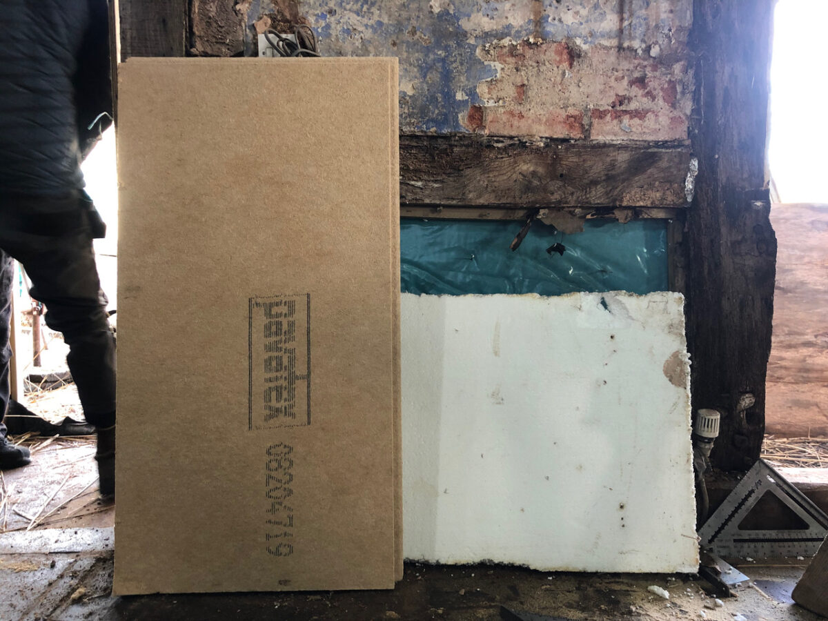 A board of insulation stands upright against a white plaster board behind it, with a fire damaged timber frame behind them both. Part of repairs to a fire damaged cottage, creating breathable construction to protect the historic fabric. Communion Architects, Hereford, Herefordshire.