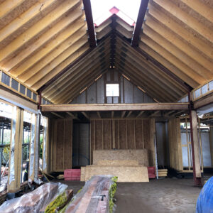 interior of a part constructed house, interior pitched timber rood with beams and boards exposed - the peak of the pitch roof is open for a future window. The sides are built with breeze blocks, and timber columns with space for floor to ceiling windows along the left hand wall. New House, New Dwelling, communion architects Hereford, Herefordshire.