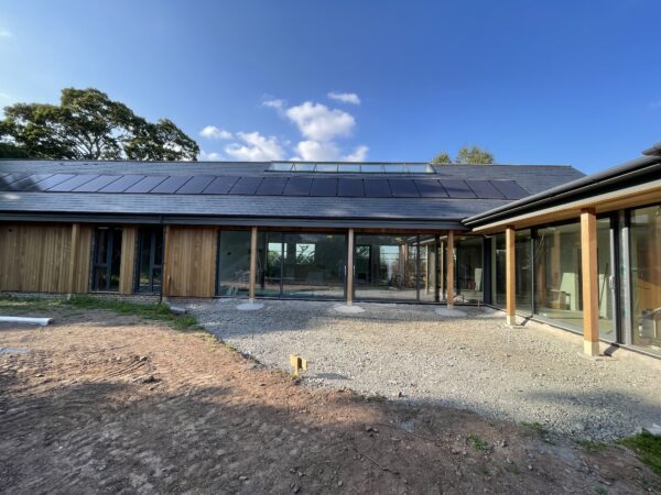 a L shaped house, single storey with a slate roof, full height glazing for the walls and timber columns supporting overhanging eaves. Communion Architects, Hereford.