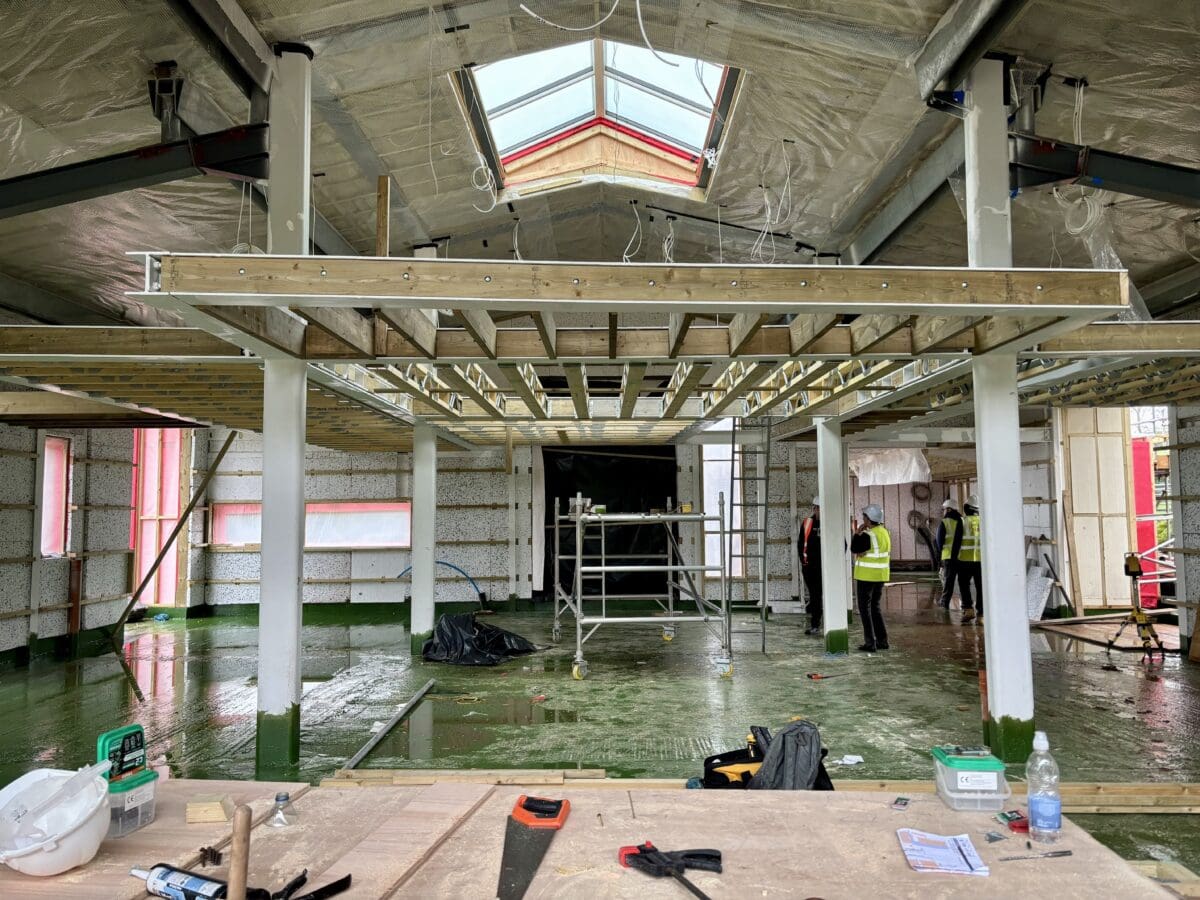 The interior of a steel framed construction showing steel timbers, a raised mezzanine platform and large glazed skylight. Communion Architects Hereford